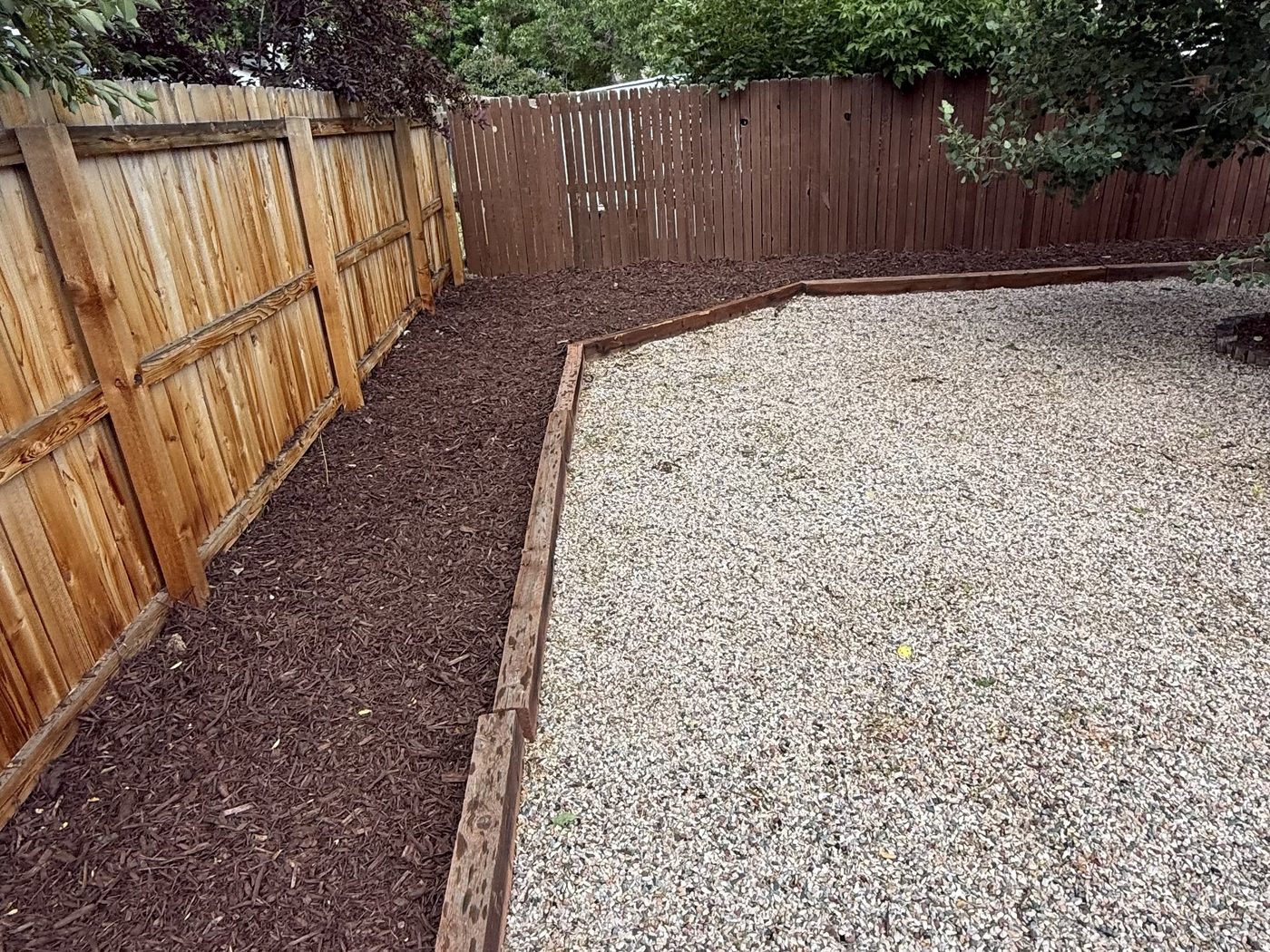 Freshly installed dark mulch bed along a fence